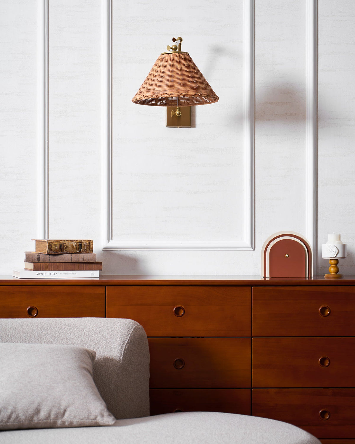 Folded close to the wall, this Clérachic rattan wall light hangs above a walnut chest of drawers on a white panelled wall.