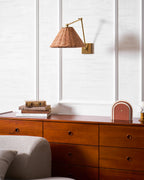 The arm of this Clérachic rattan wall light sits angled to the right, above a wooden chest with books and a small lamp.