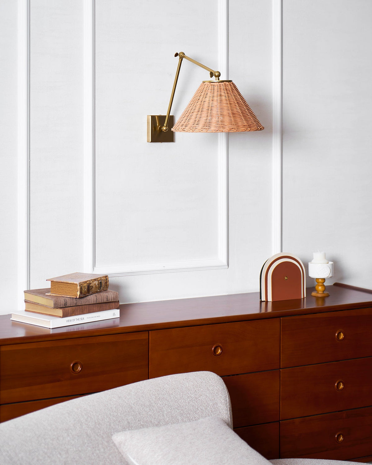 With the arm turned to the left, this Clérachic rattan cone shade hangs above a cherry chest of drawers and a grey sofa.