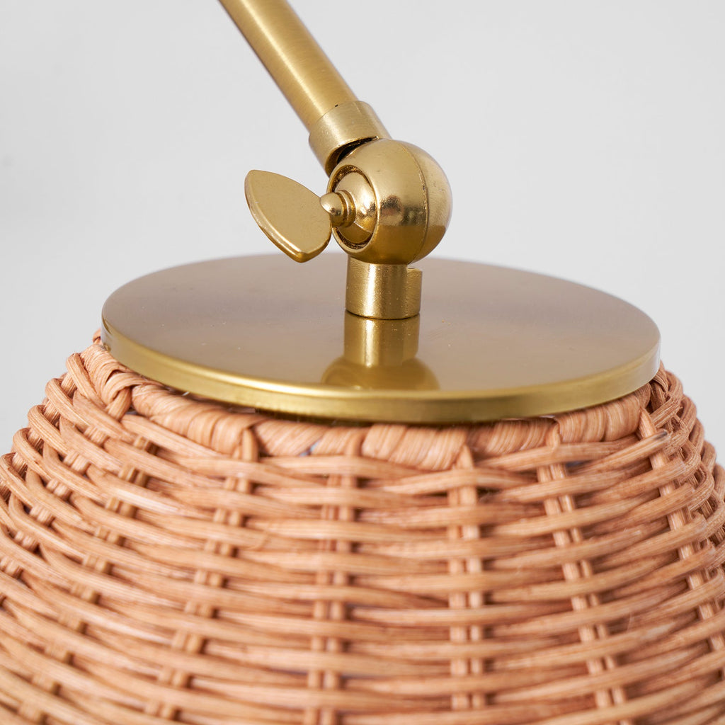 Close view of the woven rattan shade top and the gold cap and pivot joint on this Clérachic wall light.