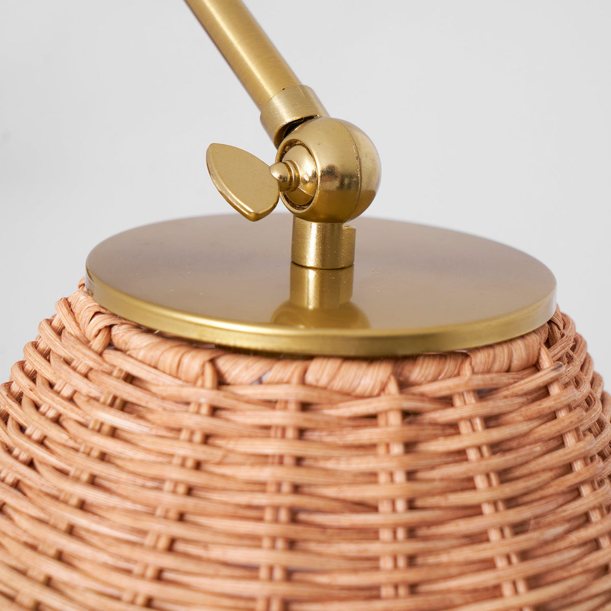 Close view of the woven rattan shade top and the gold cap and pivot joint on this Clérachic wall light.