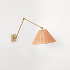 The arm on this Clérachic wall light bends down to a rattan cone shade, against a plain white wall with the gold plate at left.