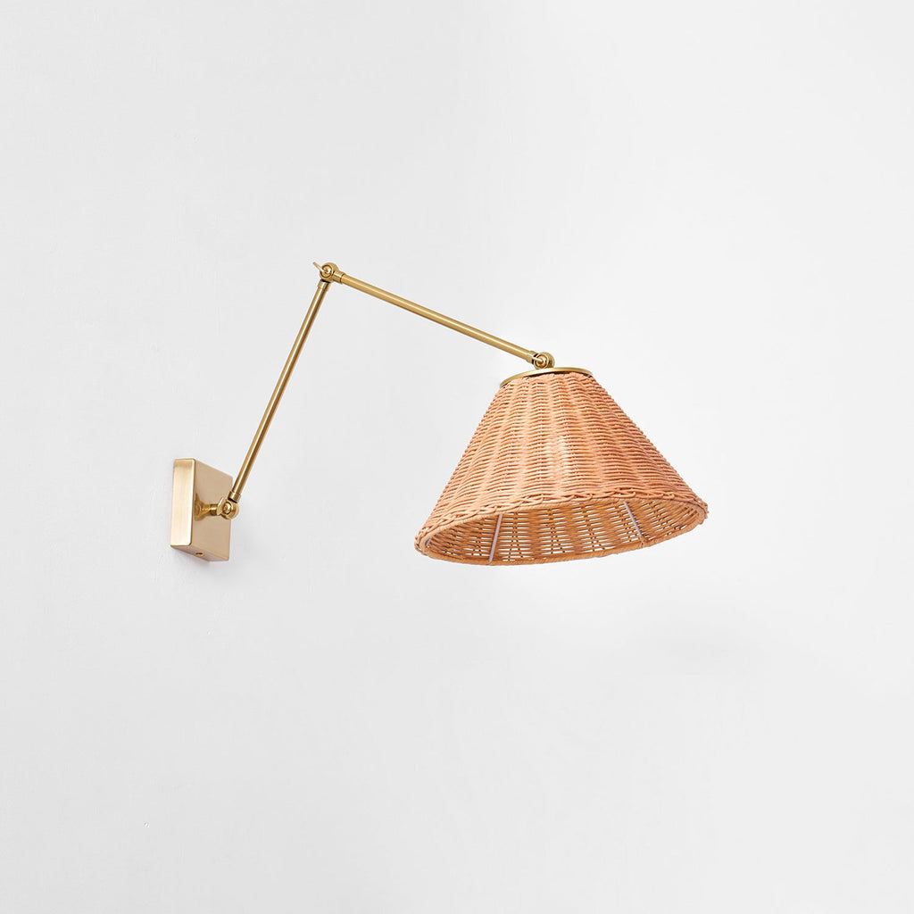 From slightly below, the open underside of the woven rattan shade of this Clérachic wall light, hung on a long gold arm.
