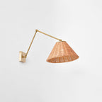 From slightly below, the open underside of the woven rattan shade of this Clérachic wall light, hung on a long gold arm.