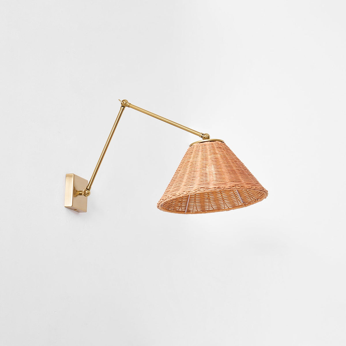 From slightly below, the open underside of the woven rattan shade of this Clérachic wall light, hung on a long gold arm.
