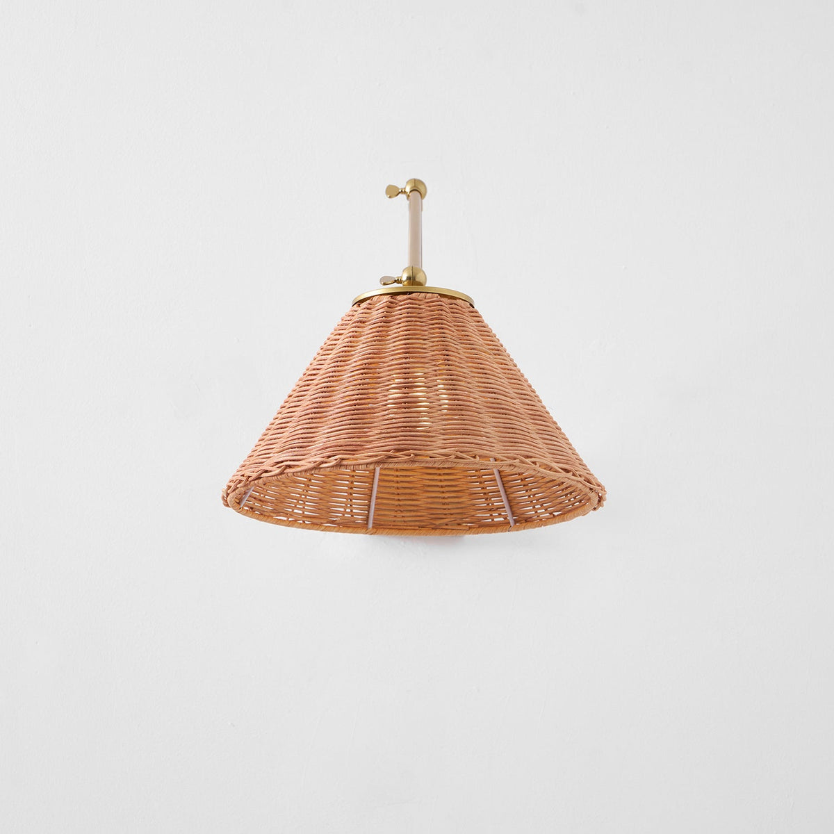 A full underside view of the woven rattan cone shade on this Clérachic wall light, with the gold arm folded above it.