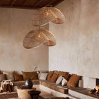 Two Clérachic rattan wave pendants hung at different heights in a corner living room, above a low sofa with rust and cream cushions.