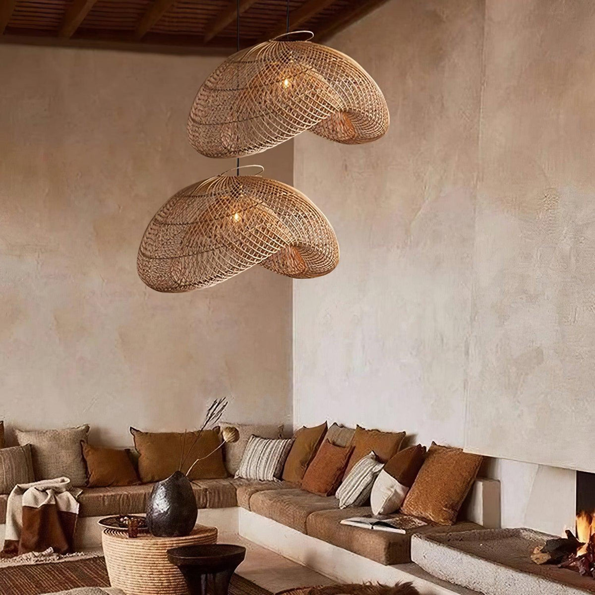 Two Clérachic rattan wave pendants hung at different heights in a corner living room, above a low sofa with rust and cream cushions.