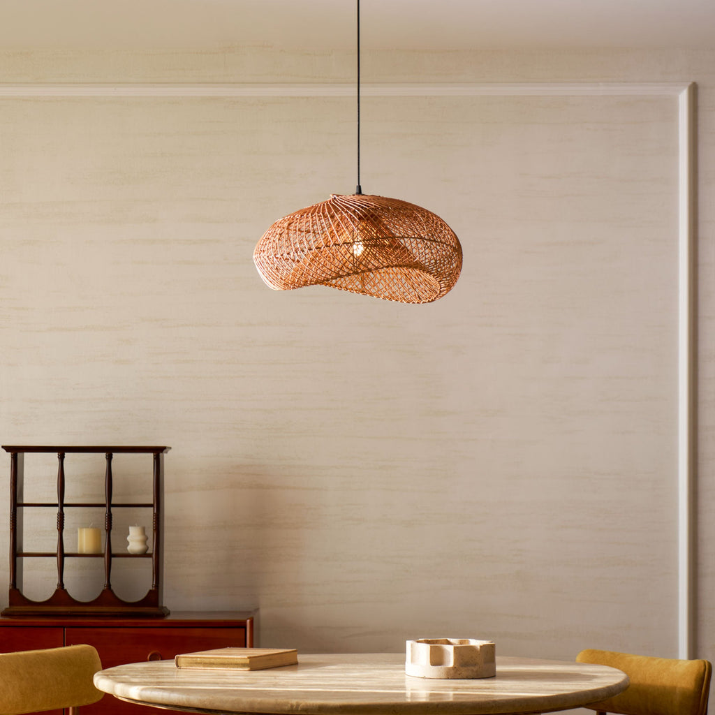 Clérachic rattan wave pendant in a pale plastered dining room, above a round stone-topped table with a small red cabinet at the side.