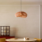 Clérachic rattan wave pendant in a pale plastered dining room, above a round stone-topped table with a small red cabinet at the side.