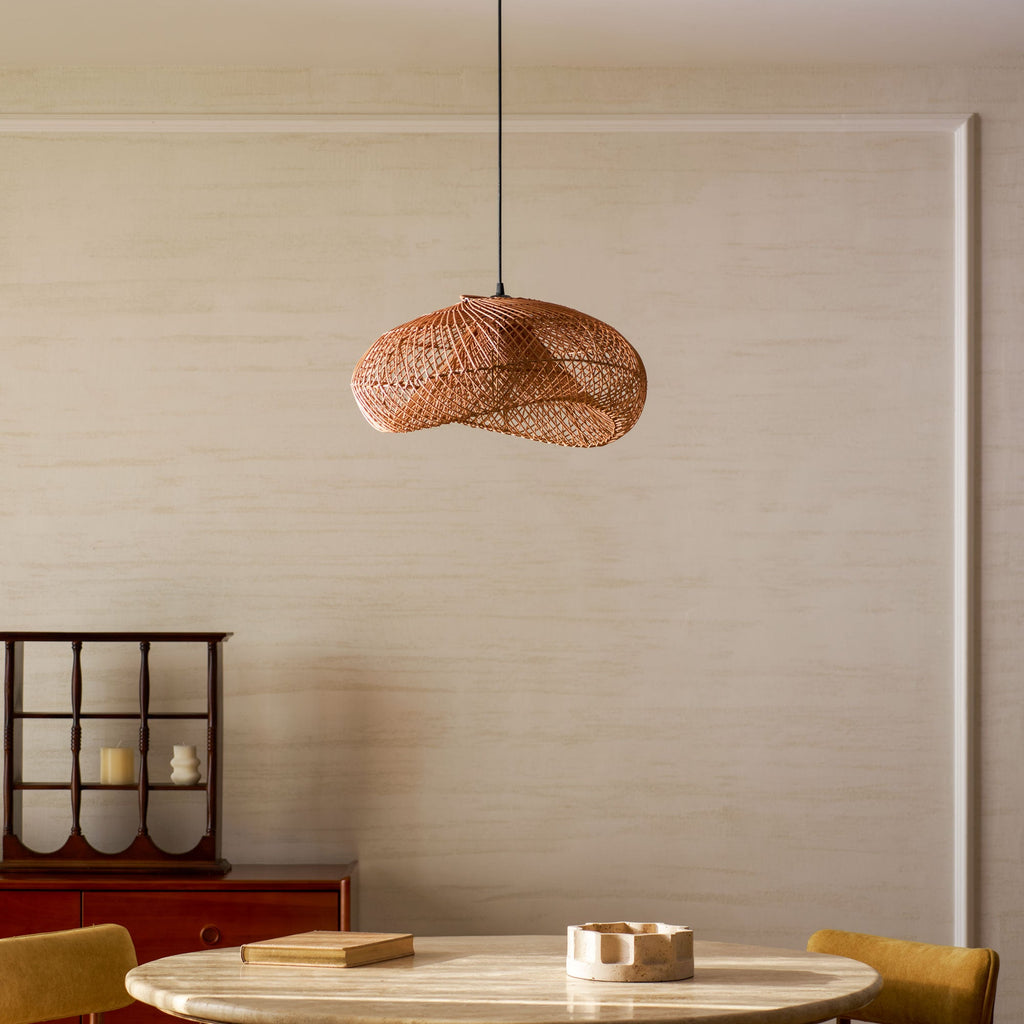 A Clérachic rattan pendant with a twisting woven shade, seen from slightly below against a cream panelled wall and a red sideboard.