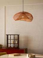 Lit Clérachic rattan wave pendant above a round table, with a glazed red cabinet holding candles on the left of the room.