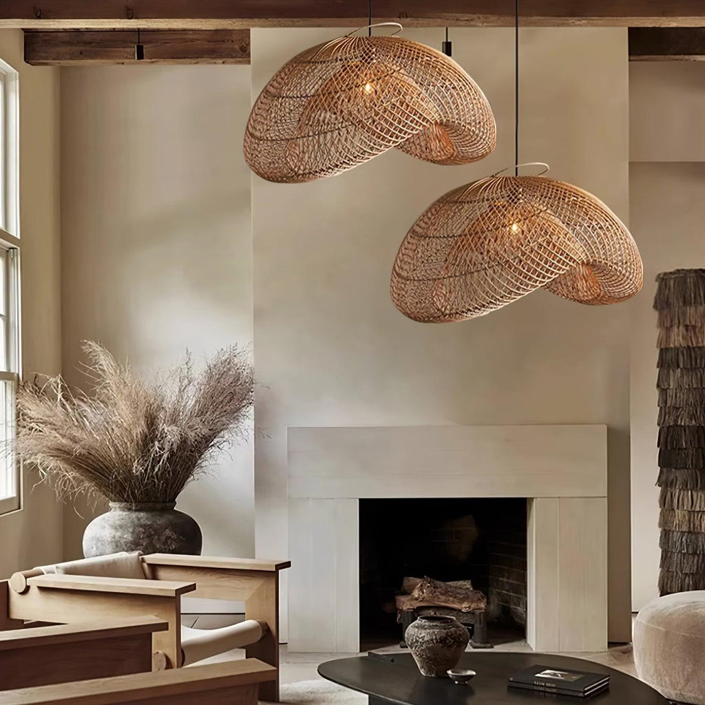 Two Clérachic rattan pendants above a stone fireplace, with dried pampas grass in a vase and wooden armchairs in a calm living room.