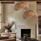 Two Clérachic rattan pendants above a stone fireplace, with dried pampas grass in a vase and wooden armchairs in a calm living room.