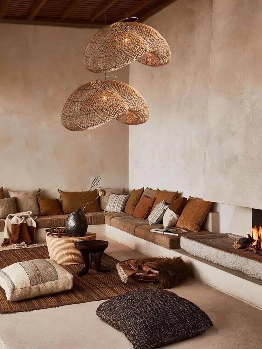 Two Clérachic rattan pendants in a tall room with a lime-washed wall, a sunken sofa, a fire and floor cushions below.