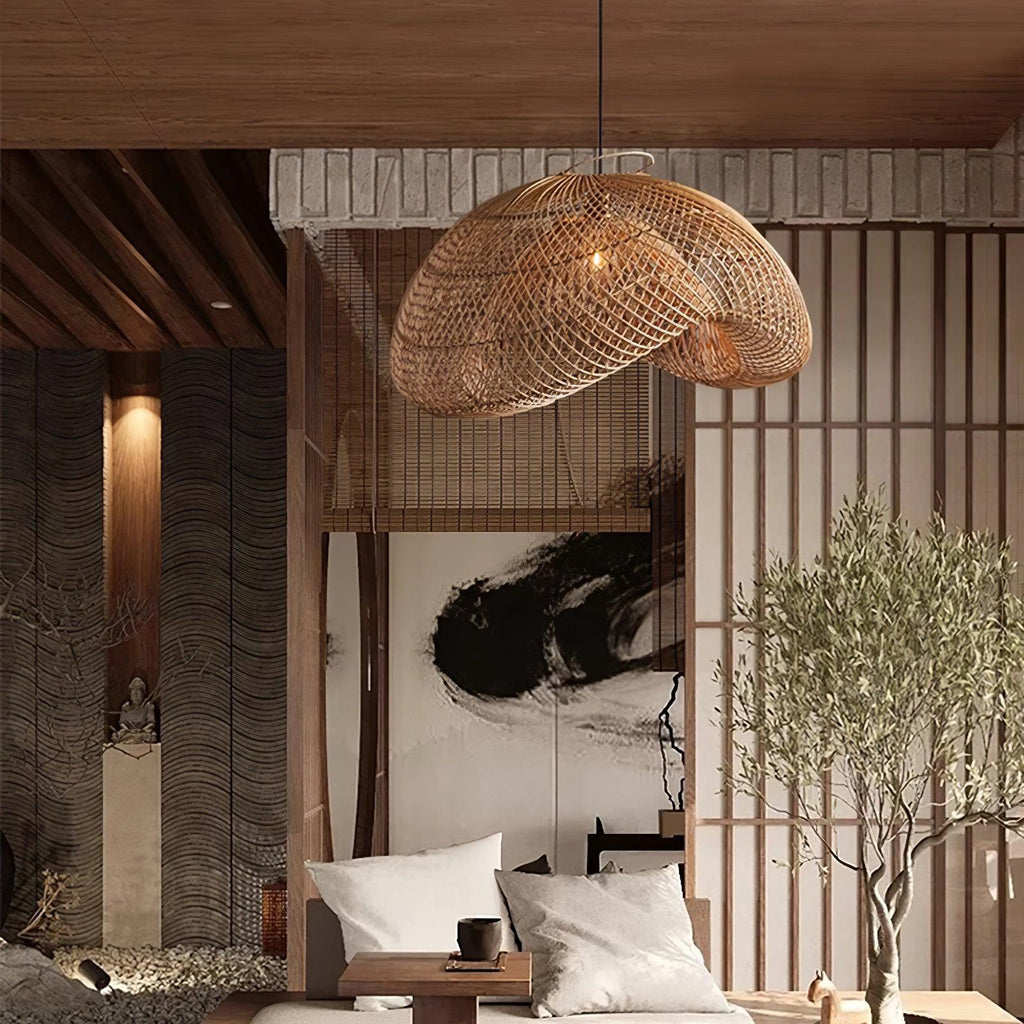 A Clérachic rattan pendant hanging in front of a slatted screen and olive tree, over a low seat with white cushions.