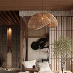A Clérachic rattan pendant hanging in front of a slatted screen and olive tree, over a low seat with white cushions.