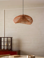 Clérachic rattan pendant above a round table with a stone bowl and a book, in a cream room with a red cabinet on the left.