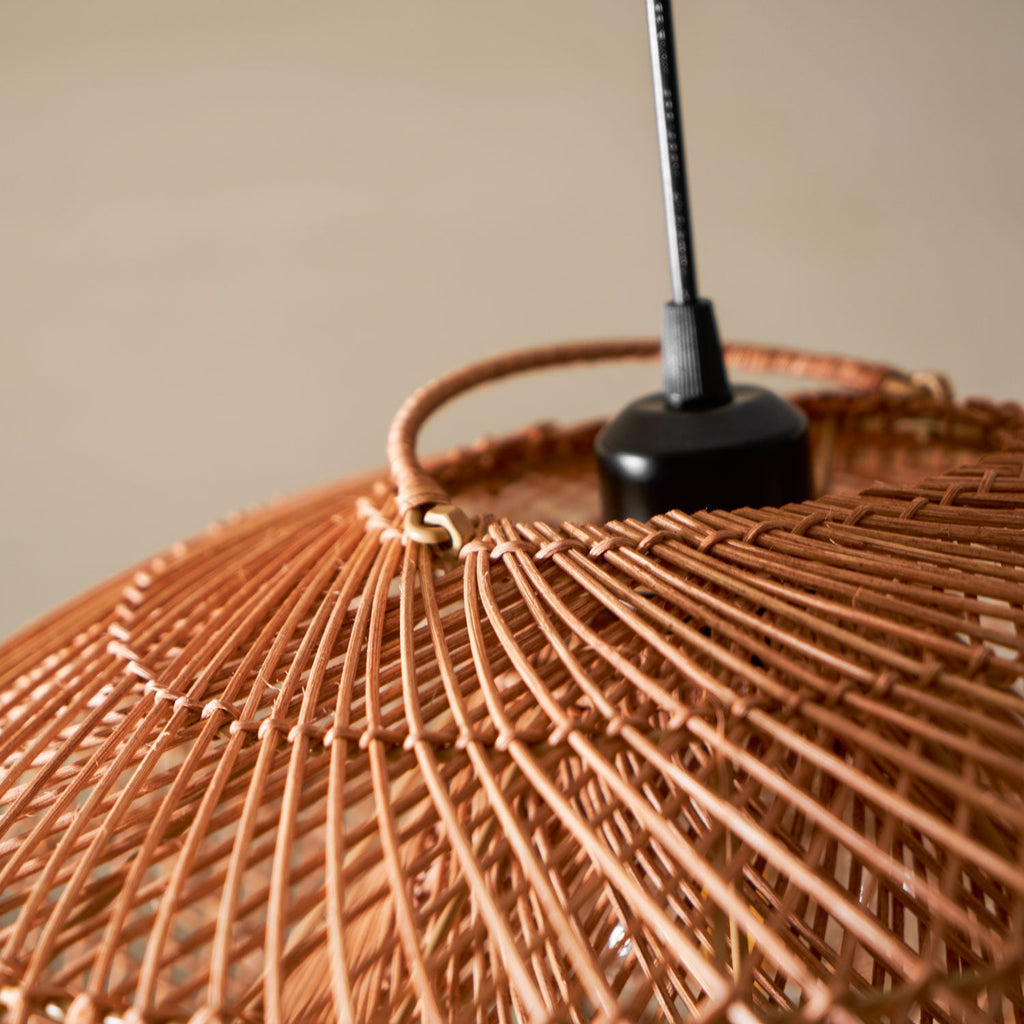 Close view of the black cord holder and the woven cane struts at the top of this Clérachic pendant, against a beige wall.