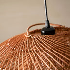 Close view of the black cord holder and the woven cane struts at the top of this Clérachic pendant, against a beige wall.