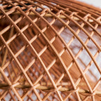 Very close view of the crossing cane strands in the woven shade of this Clérachic pendant, with a blurred wall behind.