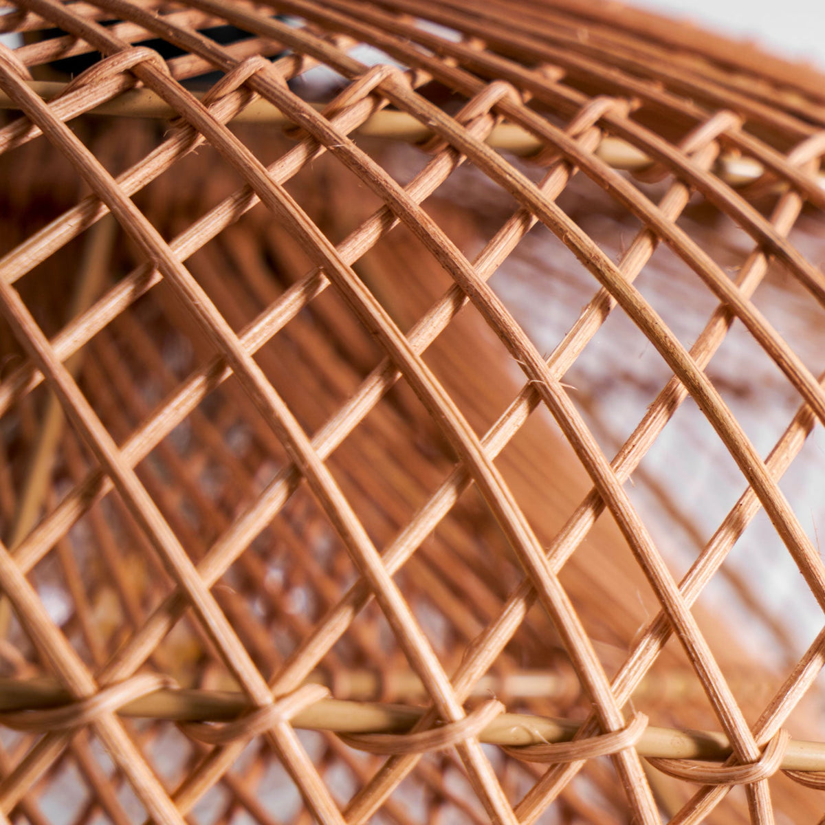 Very close view of the crossing cane strands in the woven shade of this Clérachic pendant, with a blurred wall behind.