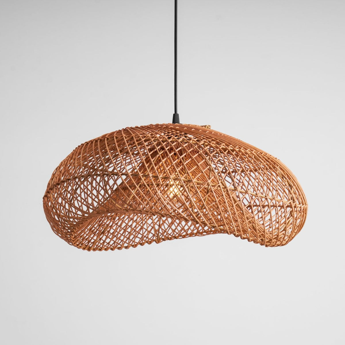 Clérachic rattan wave pendant on a pale grey backdrop, seen from a slight angle with the open weave catching the light.
