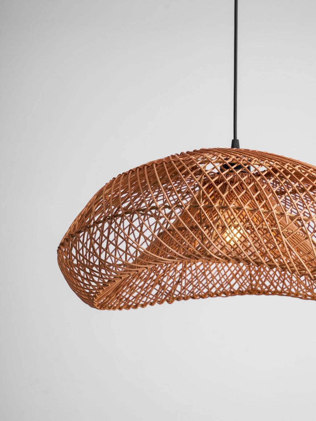 Cropped view of the woven wave shade on this Clérachic pendant, with a warm bulb inside and the black cord at the top.