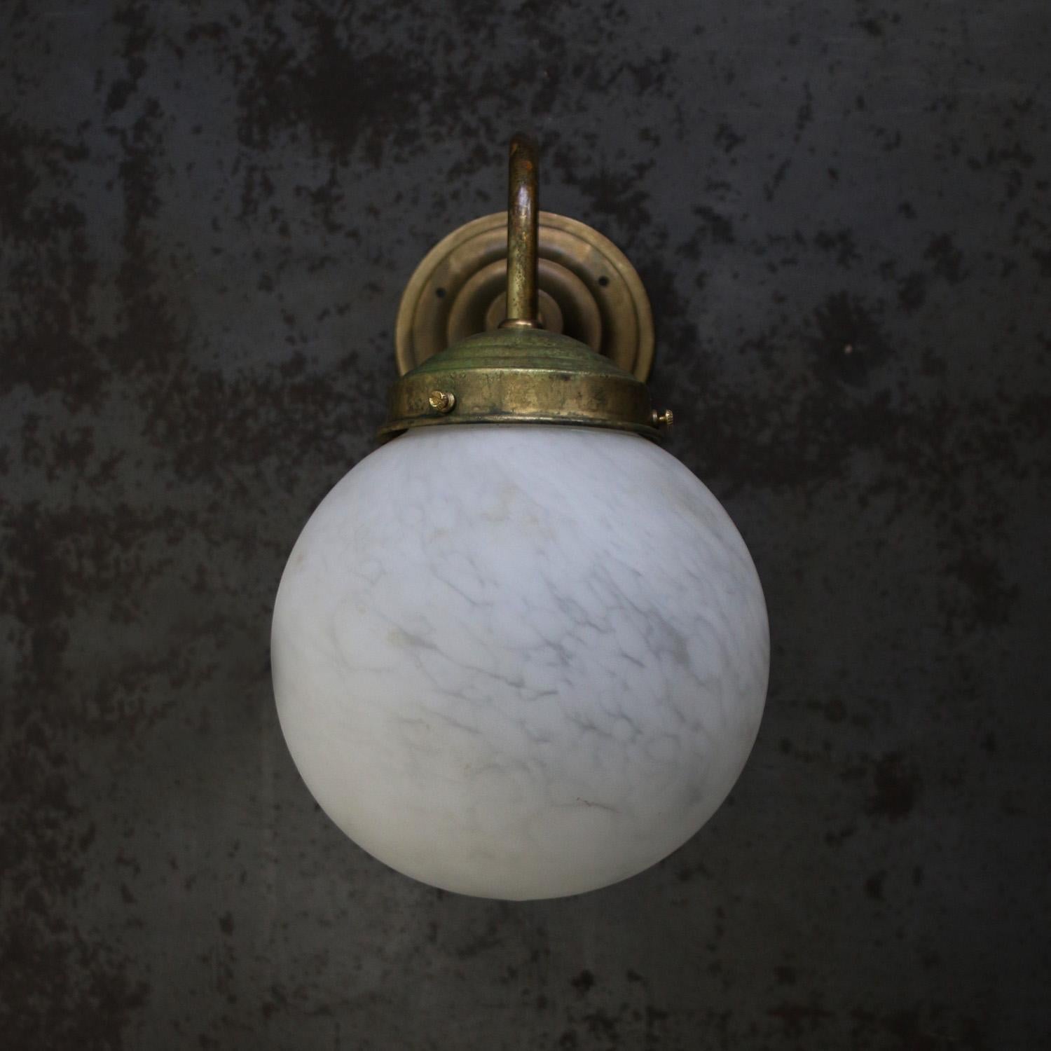 The Clérachic sconce seen head on, its brass gallery ring and fixing screws sitting neatly on top of the globe.