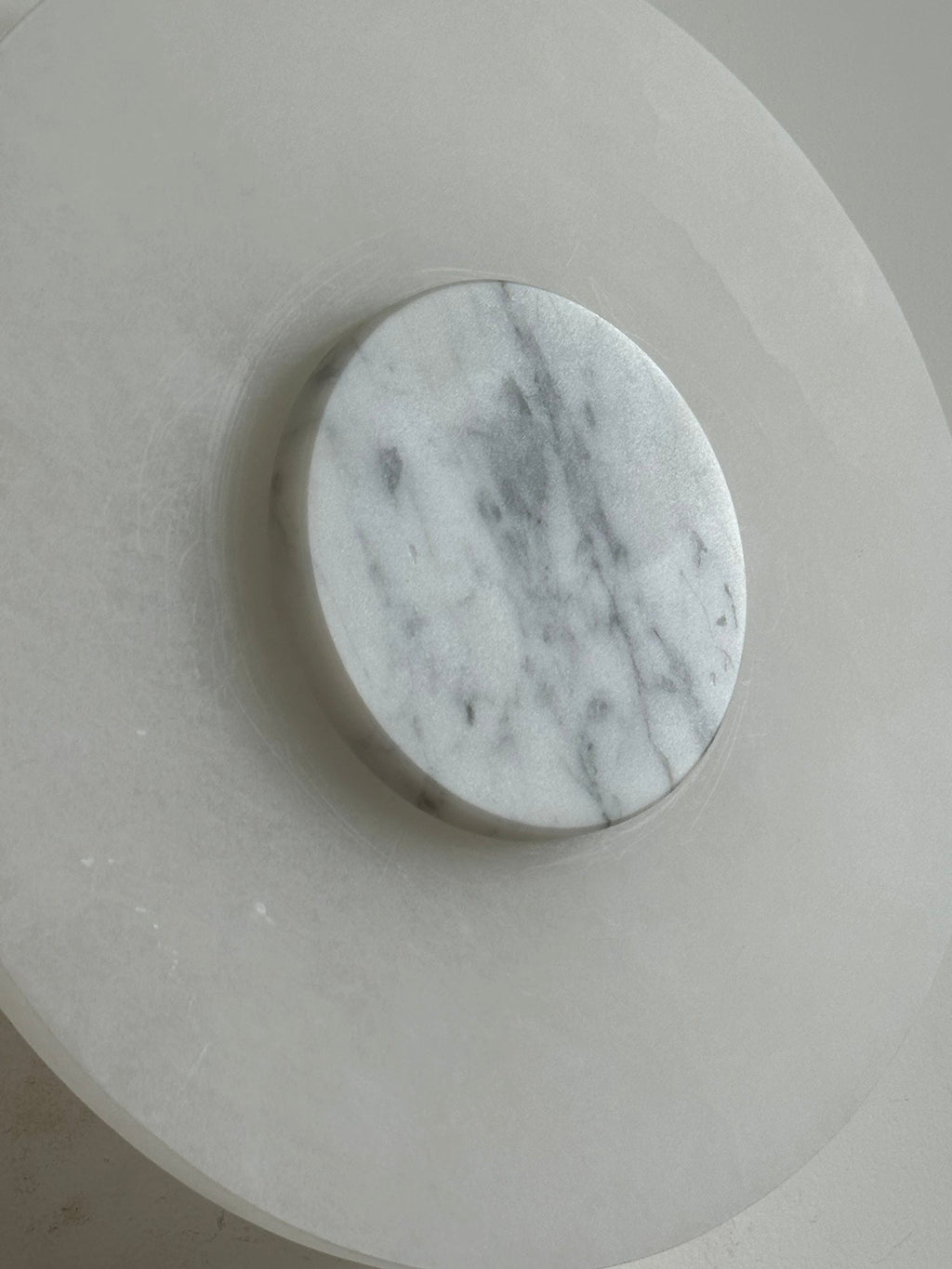 Clérachic wall lamp in close-up, its grey-veined white marble disc standing proud of the milky alabaster backplate.
