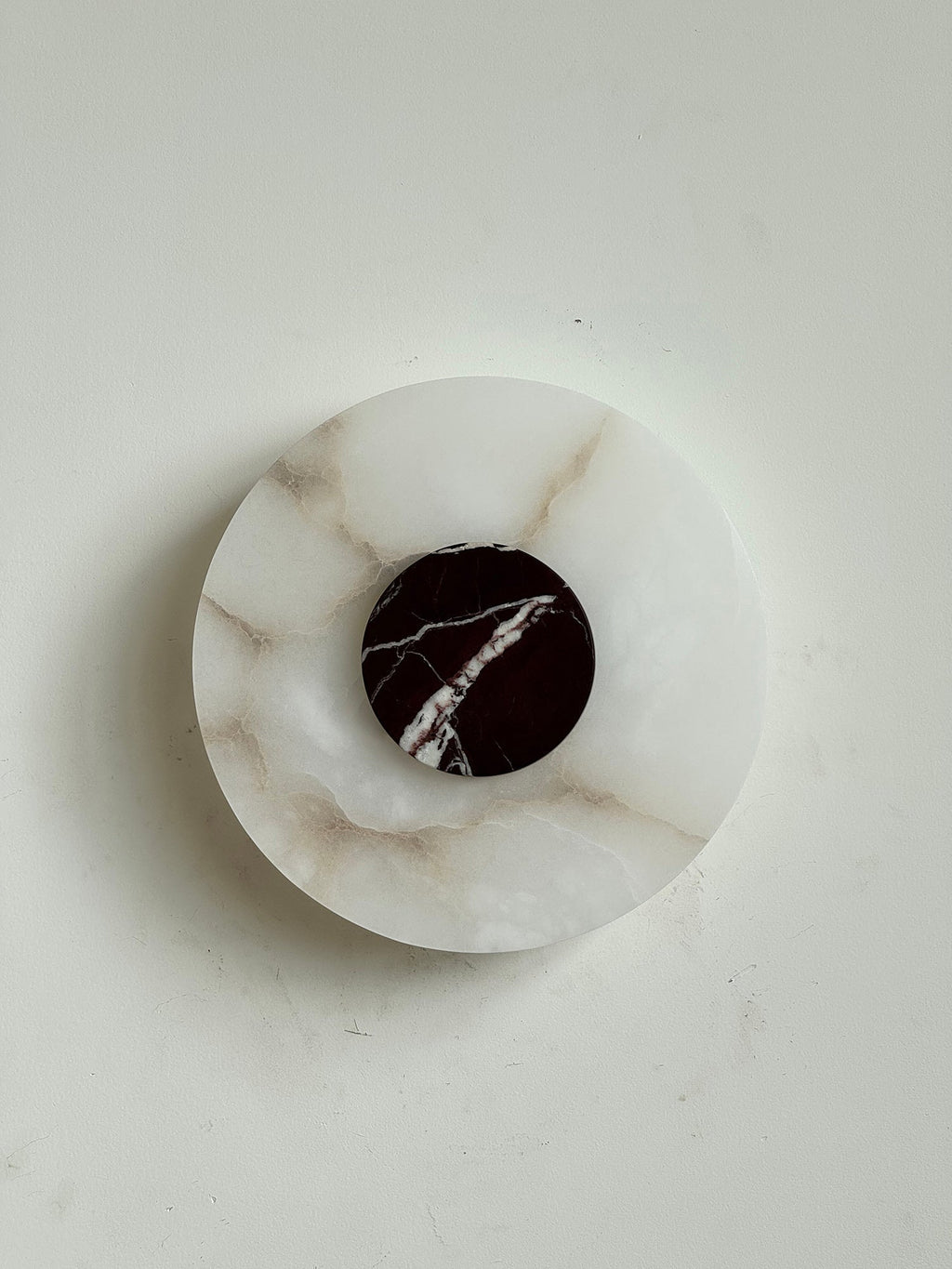 The Clérachic wall lamp from above, honey-veined alabaster carrying a burgundy marble disc split by a single white vein.