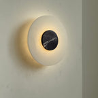 Clérachic wall lamp lit at an angle, the cream alabaster plate glowing while the dark marble disc stays in shadow.