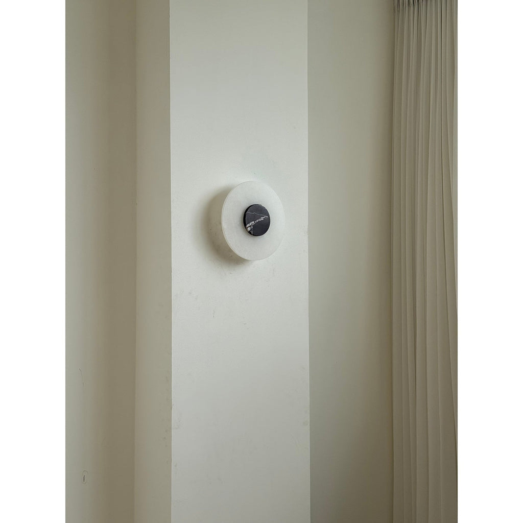 The Clérachic wall lamp unlit on a narrow plaster pier beside a floor-length pleated curtain, showing its modest scale.