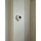 The Clérachic wall lamp unlit on a narrow plaster pier beside a floor-length pleated curtain, showing its modest scale.