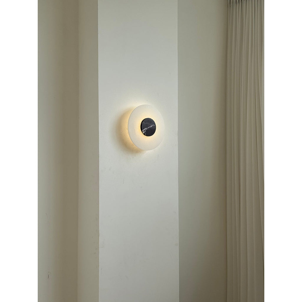 Clérachic wall lamp switched on in a room setting, a soft ring of light circling its dark marble centre.