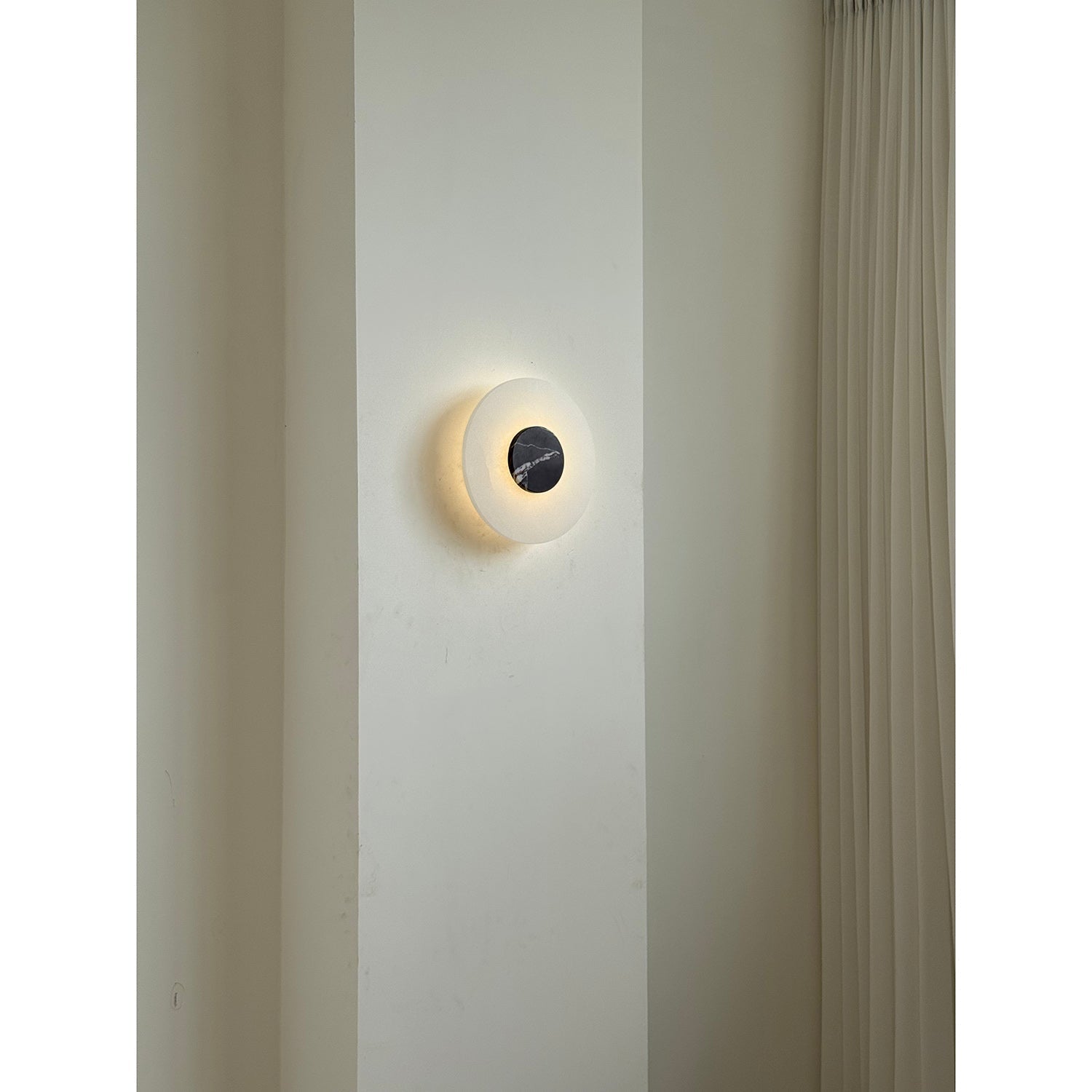 Clérachic wall lamp switched on in a room setting, a soft ring of light circling its dark marble centre.