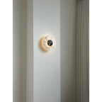 The Clérachic wall lamp off against a pale pier, its veined alabaster plate catching daylight beside a pleated curtain.