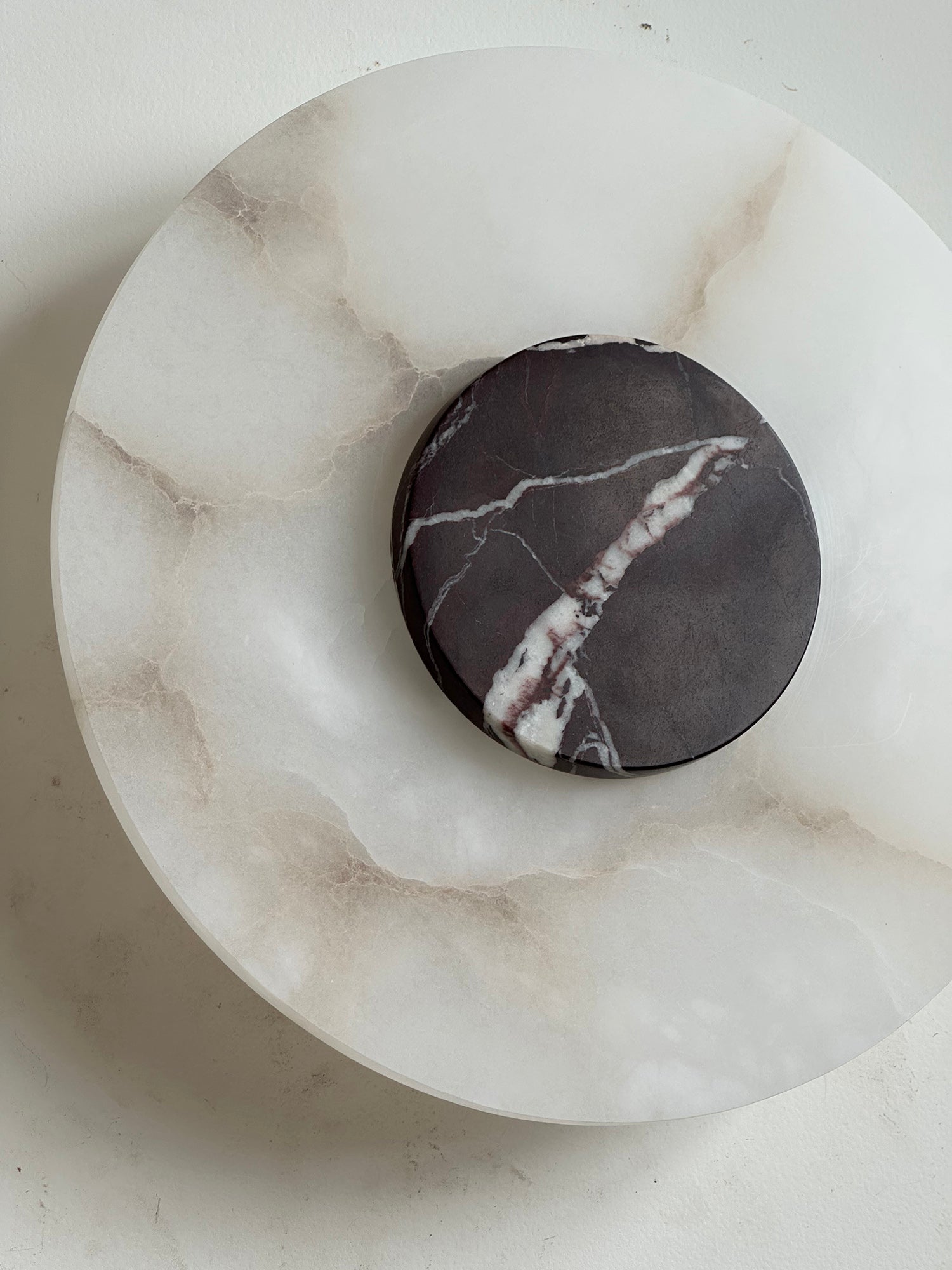 The Clérachic wall lamp close up at an angle, heavy brown veining in the alabaster under a plum-toned marble disc.