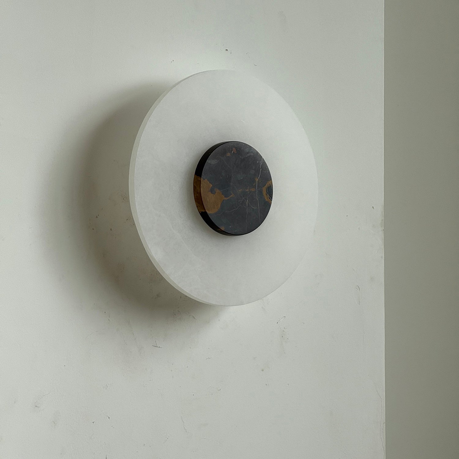 Clérachic wall lamp unlit at three-quarters, its black marble disc streaked with ochre gold over pale alabaster.