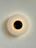 The Clérachic wall lamp lit square-on, warm light escaping around a black and gold marble disc.