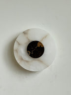 Clérachic wall lamp unlit and angled, tan veins drifting through the alabaster below a gold-flecked black marble disc.