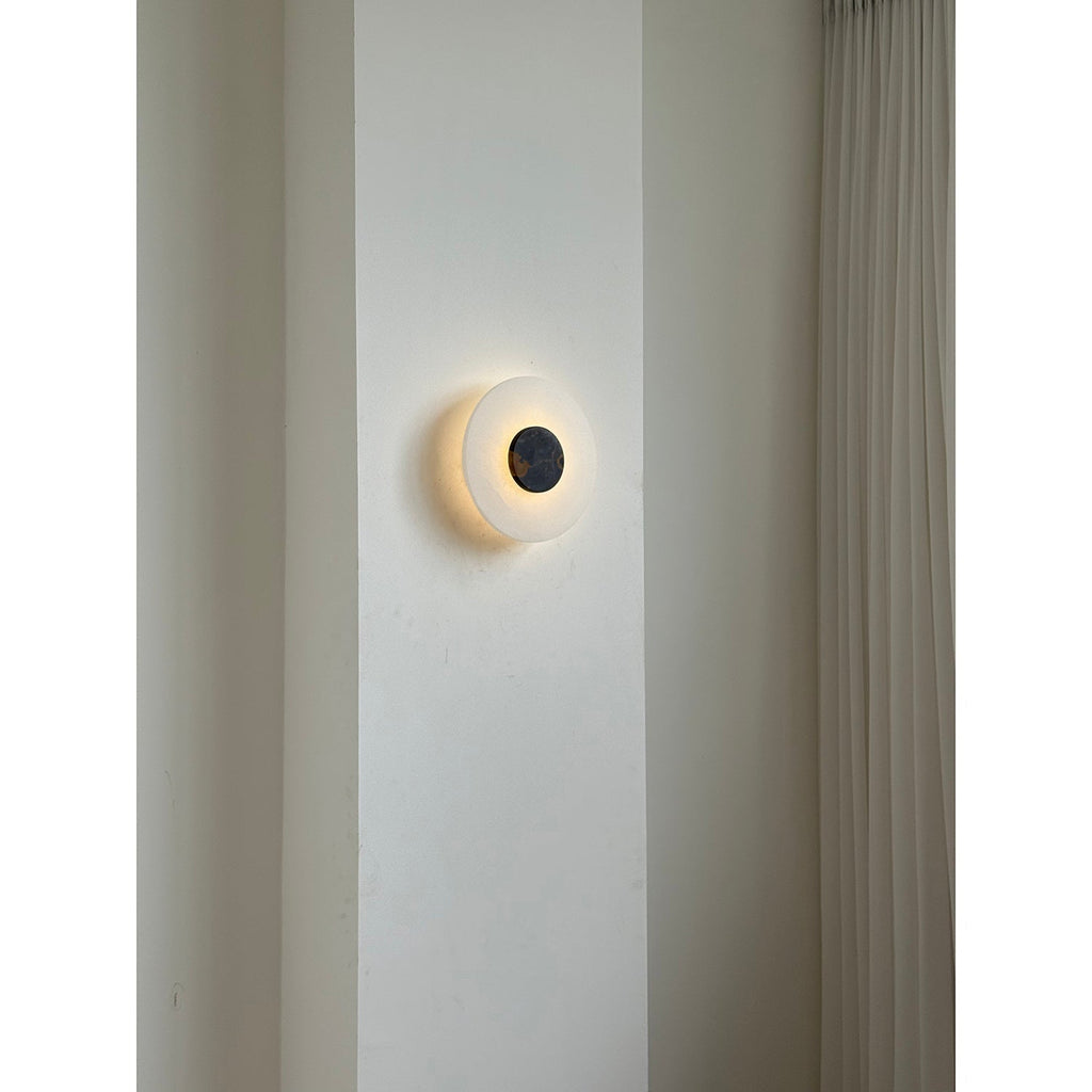 The Clérachic wall lamp glowing softly on a plaster pier, its dark centre disc reading like a small eclipse.