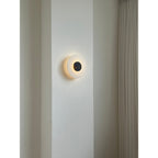 The Clérachic wall lamp glowing softly on a plaster pier, its dark centre disc reading like a small eclipse.