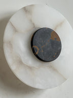 The Clérachic wall lamp in macro, a rust-gold veined black marble disc seated proud of the cloudy alabaster plate.