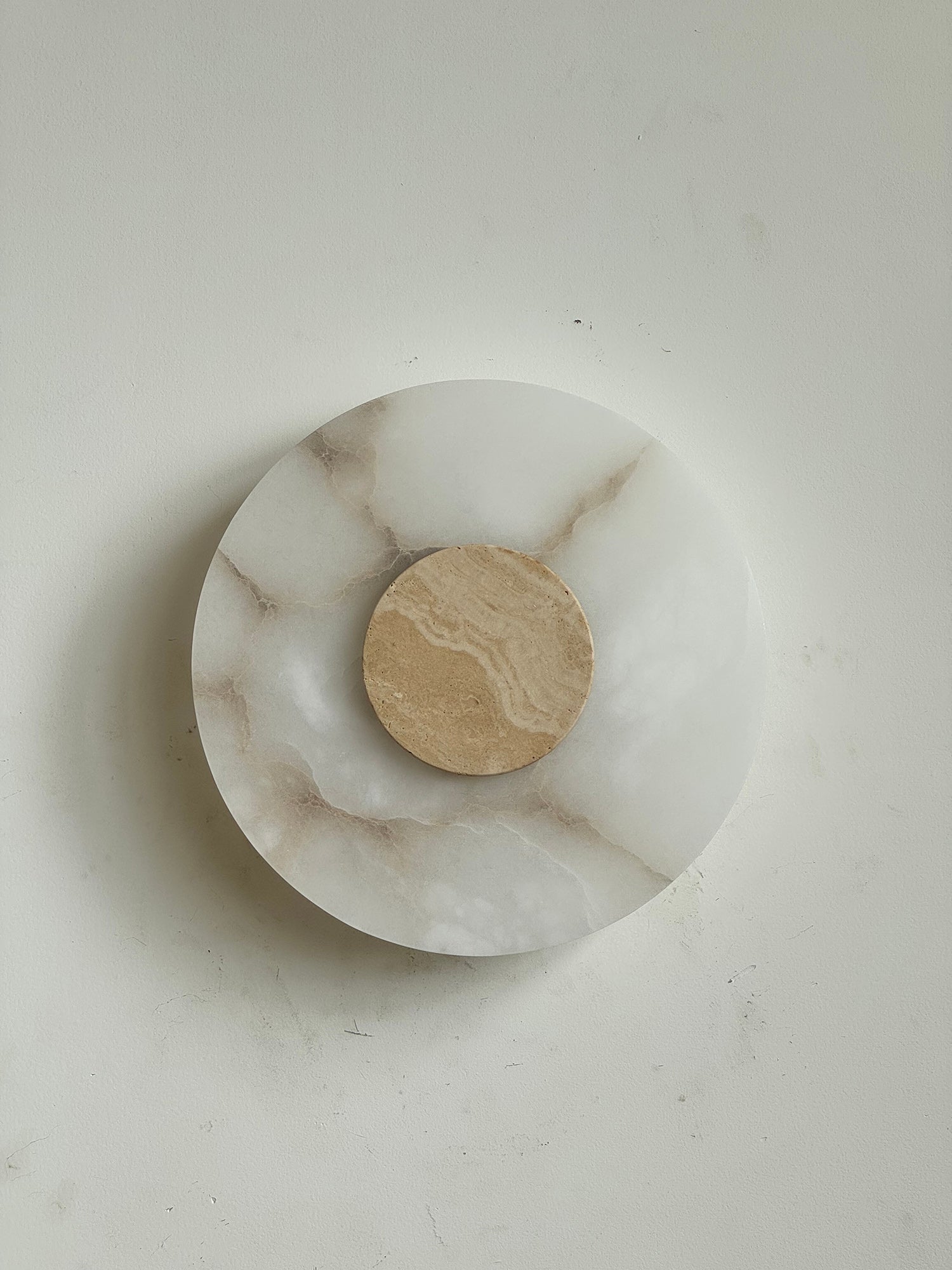 The Clérachic wall lamp seen square-on and unlit, warm travertine disc centred on brown-veined alabaster.