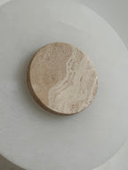 Clérachic wall lamp in macro, banded travertine grain running across the disc that sits on the alabaster plate.