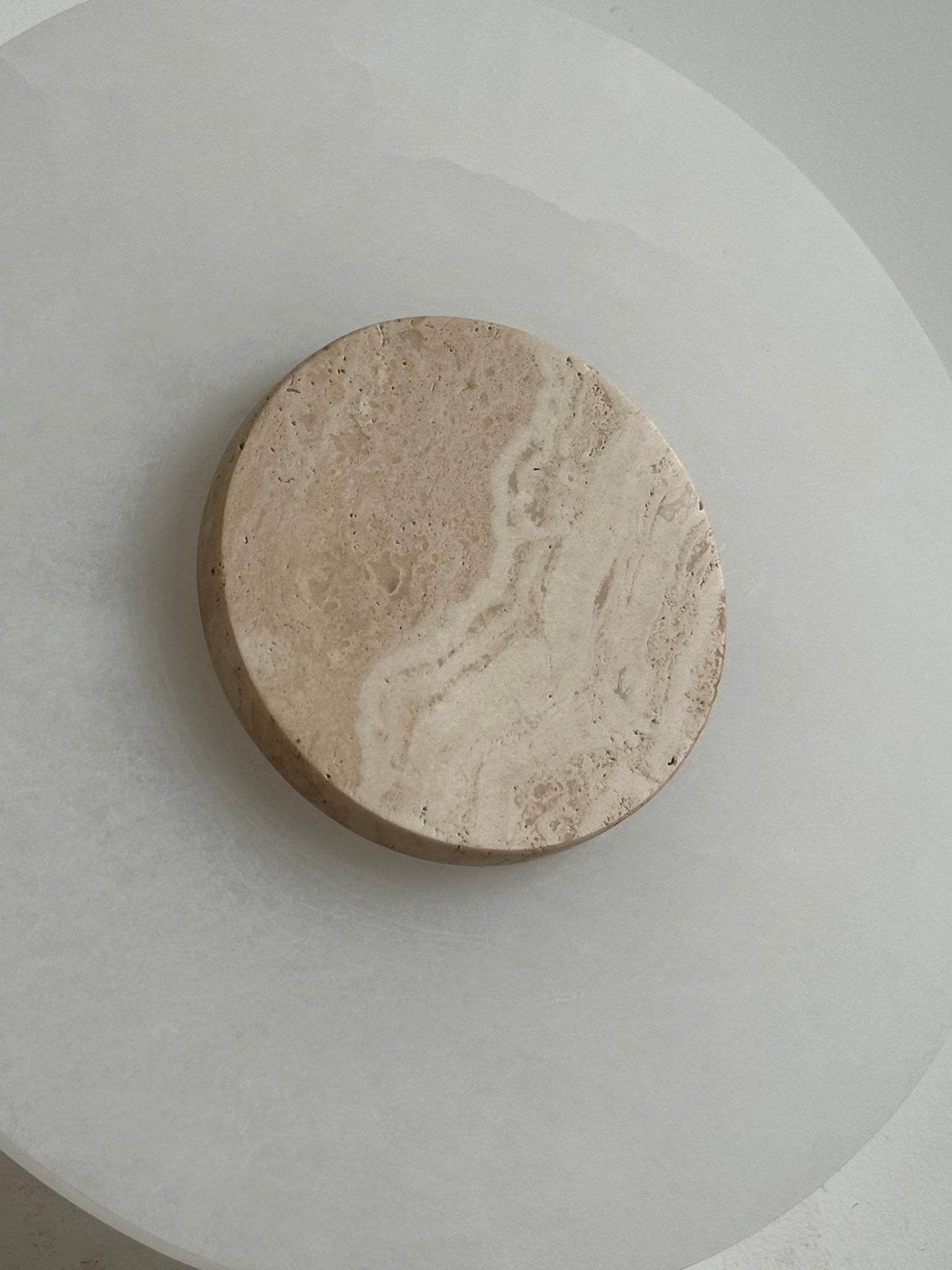 Clérachic wall lamp in macro, banded travertine grain running across the disc that sits on the alabaster plate.