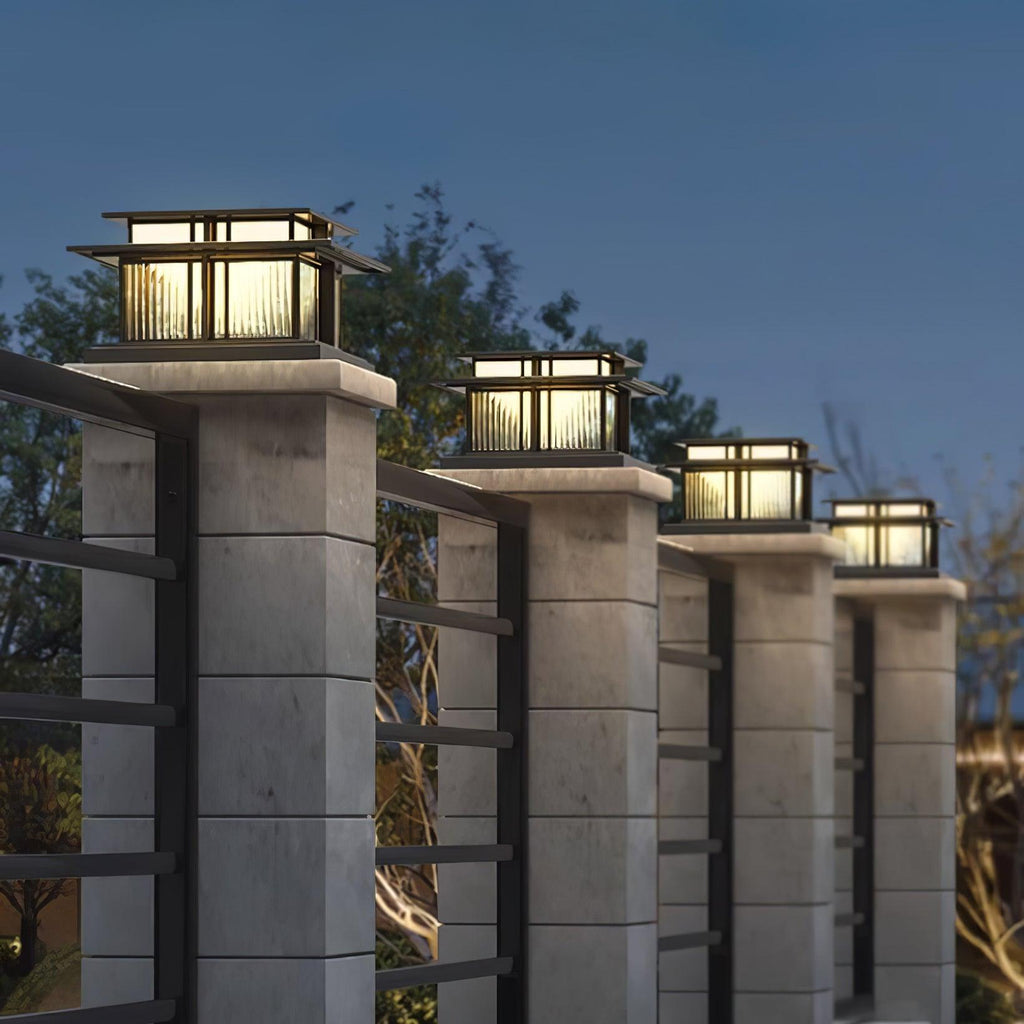 Clérachic Ray pillar lights capping stone gate posts at dusk with a slatted fence between.