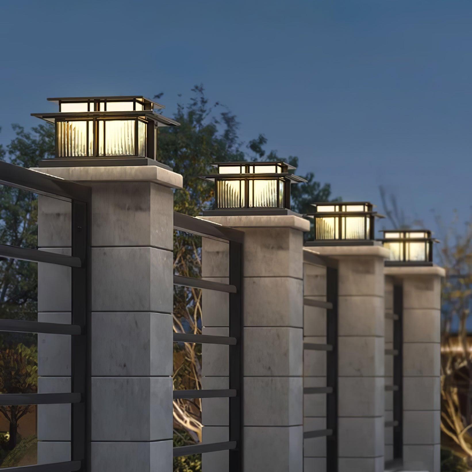 Clérachic Ray pillar lights capping stone gate posts at dusk with a slatted fence between.