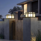 Two Clérachic Ray pillar lights lit on concrete gate piers outside a modern house at dusk.